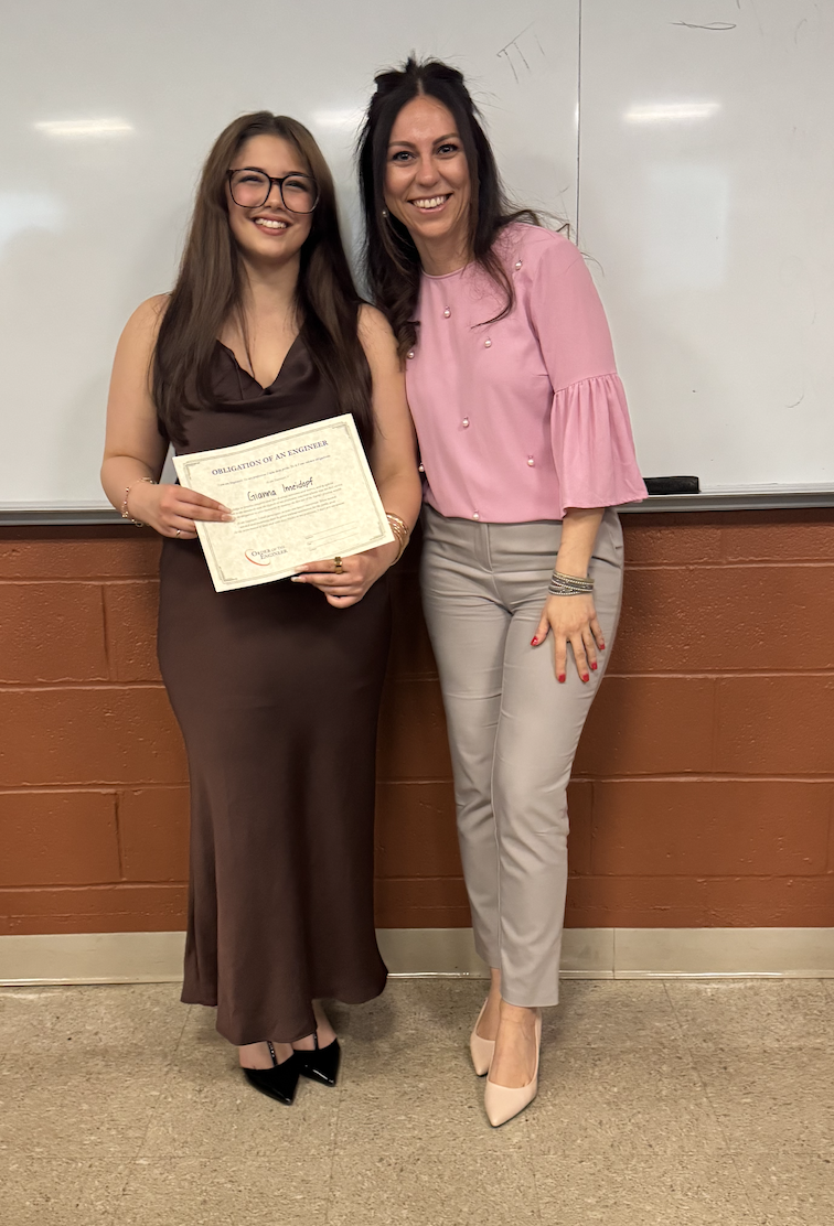 Gianna holding her Engineering Ring Ceremony certificate with a professor